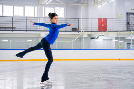 young girl figure skater is skating on the ice with a smile on her face. She is wearing a blue tracksuit.の写真素材
