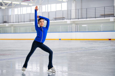 young girl figure skater is skating on the ice with a smile on her face. She is wearing a blue tracksuit.の写真素材