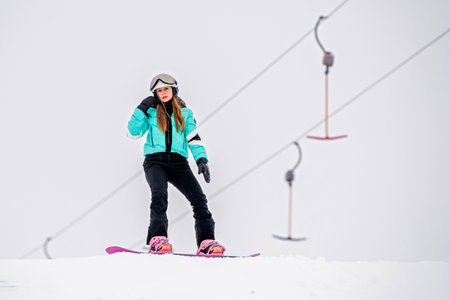 Young female snowboarder gliding down a snowy slope, dressed in stylish winter gear. Exciting winter sports and outdoor adventure.の写真素材