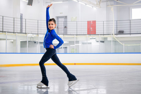 young girl figure skater is skating on the ice with a smile on her face. She is wearing a blue tracksuit.の写真素材