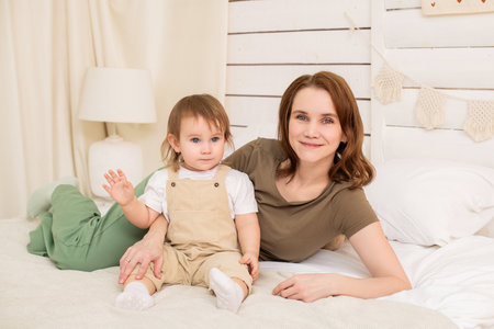 cheerful baby plays on a cozy bed with a loving mother. Harmonious development and care in the atmosphere of home and family.の写真素材