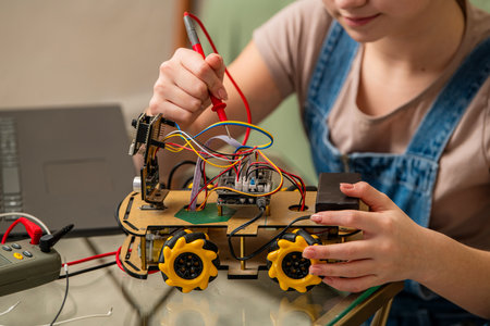 Young individual working on a DIY motorized robot car, testing circuits with a multimeter. Focusing on hands-on robotics project with visible circuit board and wheelsの写真素材