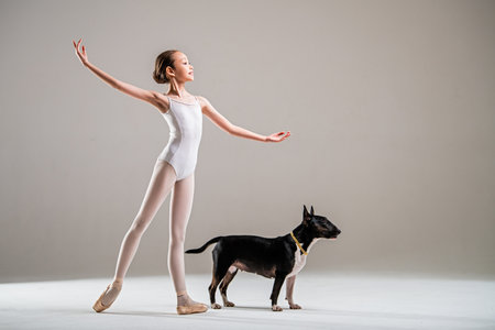 young girl poses elegantly in a ballet outfit next to a well-behaved dog. She demonstrates graceful movements illustrating the harmony between a person and a pet in a calm studio settingの写真素材