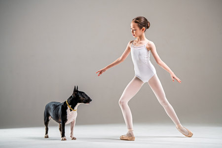 young girl poses elegantly in a ballet outfit next to a well-behaved dog. She demonstrates graceful movements illustrating the harmony between a person and a pet in a calm studio settingの写真素材