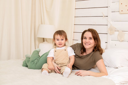 cheerful baby plays on a cozy bed with a loving mother. Harmonious development and care in the atmosphere of home and family.の写真素材