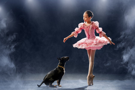 young ballerina dances in a pink tutu next to a dog. The contrast between the ballerina's sophistication and the dog's squatness.の写真素材