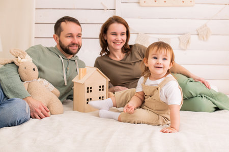 cheerful toddler plays on a cozy bed while their loving parents watch with smiles. The warm and harmonious atmosphere of the home reflects happiness and family bondingの写真素材