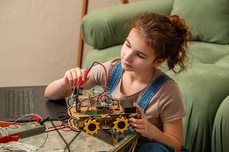 Young girl is deeply focused on assembling a robotics project. She is using electronic tools and wires at a table, demonstrating interest and concentration in a learning activityの写真素材