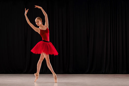 ballerina in a vibrant red dress performs a variation on stage. Capturing the grace and skill of ballet in a dynamic pose.の写真素材