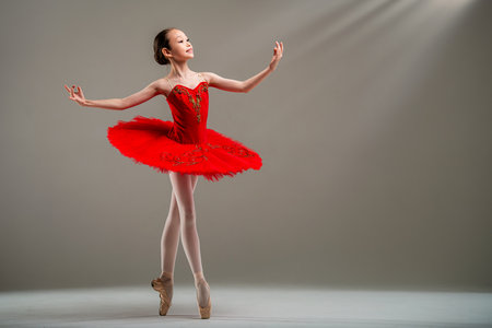 Young Japanese ballerina in red tutu and pointe shoes dances classical dance on light background.の写真素材