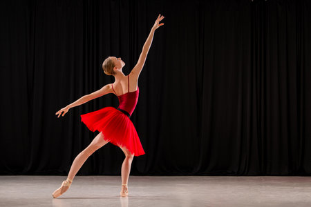 ballerina in a vibrant red dress performs a variation on stage. Capturing the grace and skill of ballet in a dynamic pose.の写真素材