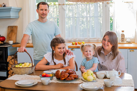 Family moment in the kitchen with a woman presenting freshly baked pastries to a father and daughter. Smiles and warmth are shared, highlighting a loving, domestic atmosphereの写真素材
