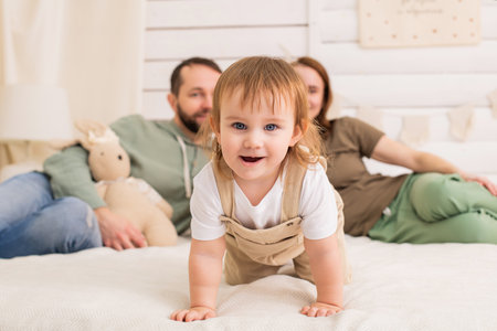 cheerful toddler plays on a cozy bed while their loving parents watch with smiles. The warm and harmonious atmosphere of the home reflects happiness and family bondingの写真素材