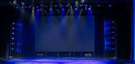 Empty theater stage illuminated with blue lighting and multiple spotlights. The scene creates an anticipation for a performance or event in a large auditorium setting.の写真素材
