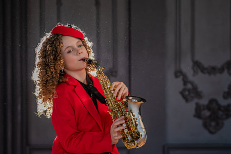 Young girl wearing a vibrant red outfit passionately plays a saxophone with eyes closed, showcasing her musical talent and concentration. Curly hair adds visual interest.の写真素材