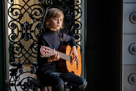 Young boy playing an acoustic guitar with a focused expression. The image captures a moment of concentration and musical engagement, set against a decorative backgroundの写真素材