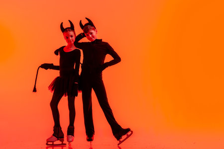 Young figure skaters perform on ice dressed as devils for Halloween against a bright orange backgroundの写真素材