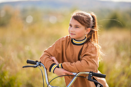 teenage girl leaning on bicycle handlebars against natural landscape with hilly terrainの写真素材