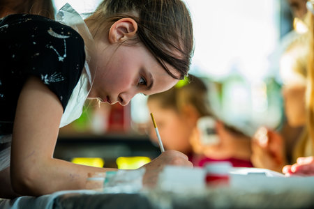 Young girl concentrating deeply while painting in an art class. Her focused expression, surrounded by art supplies, suggests dedication and creativity in learning artistic techniquesの写真素材