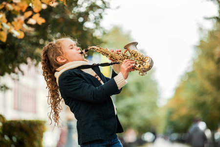 Young girl playing saxophone during an outdoor performance. Child musician learning musical instrument. Talent and hobby concept for development.の写真素材