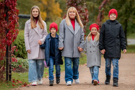 Woman and kids walking in park holding hands. Happy family in autumn with fall foliage. Unity and...