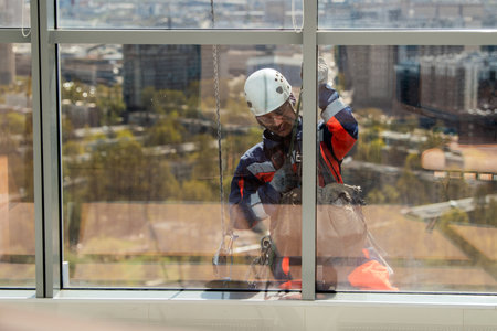 Man industrial climber or window cleaner on a rope washing skyscraper windows. High-rise work and...