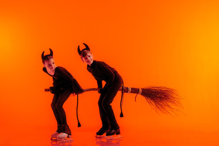 Young figure skaters perform on ice dressed as devils for Halloween against a bright orange...