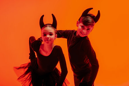 Children in devil costumes. Graceful young figure skaters in Halloween-themed costumes performing on...