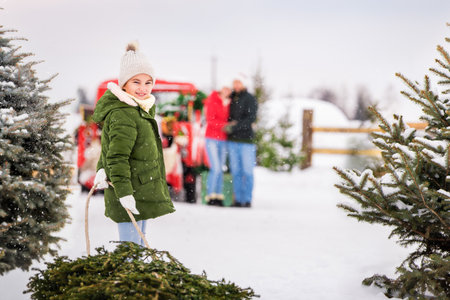 girl is carrying a Christmas tree on a sleigh to her parents, who are waiting for her near the red car.の写真素材