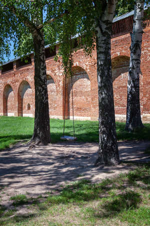Wooden swing on chains between trees in free flight against the background of the old brick Kremlin wall, Zagorsk Russia. The concept of travel, healthy lifestyle.の写真素材