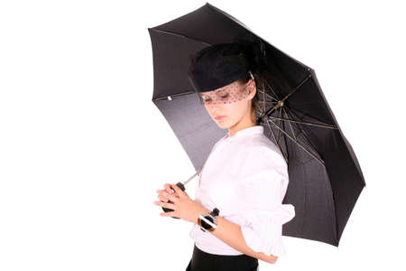 A young beautiful lady with a watch on her hand in a blak hat holding an umbrella standing over white backgroundの写真素材