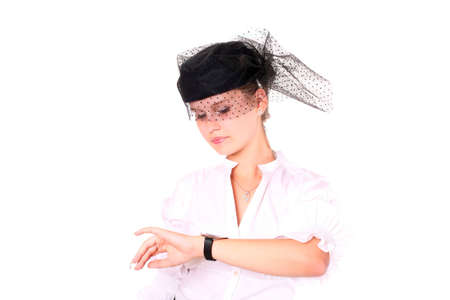 A young beautiful lady looking at her watch and wearing a black hat standing over white backgroundの写真素材