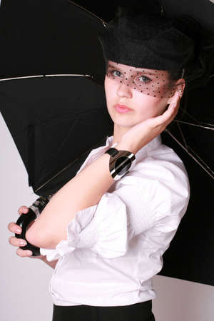 A young beautiful lady with a watch on her hand in a blak hat holding an umbrella standing over...