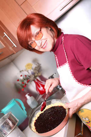 A smiling grandmother is cooking a jam tartの写真素材
