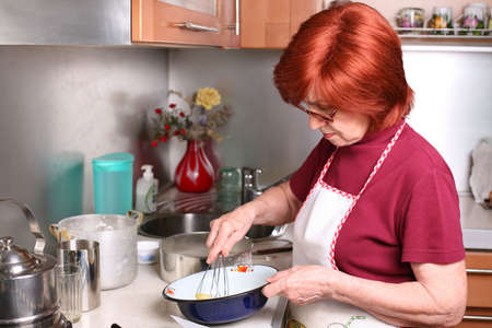 A grandmother  beats eggs in a bowlの写真素材