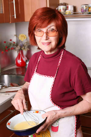 Grandmother beats eggs in a bowl and looking to cameraの写真素材