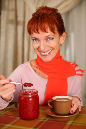 A smiling woman holding a cup of tea with raspberry jamの写真素材
