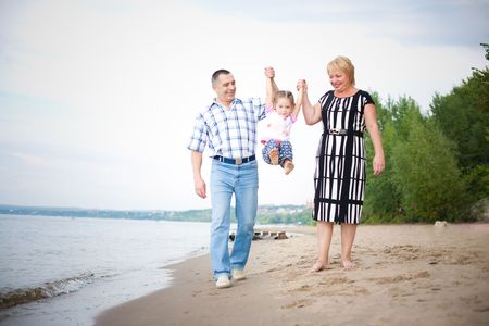 Happy grandparents walking with their grangdaughter on the beachの写真素材