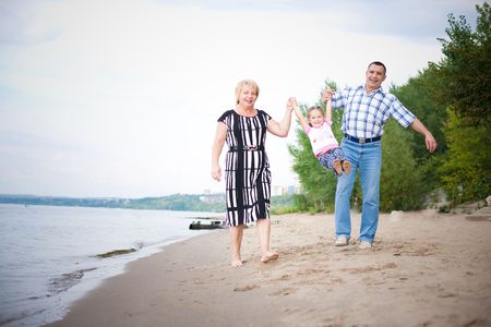 Happy grandparents walking with their grangdaughter on the beach