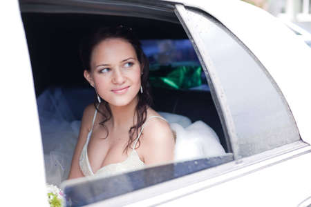 Attractive bride with a wedding bouquet sitting in the carの写真素材