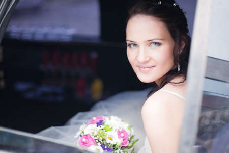 Attractive bride with a wedding bouquet sitting in the carの写真素材