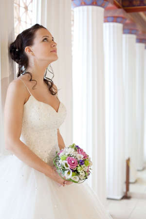Attractive bride is holding a wedding bouquet and looking upの写真素材