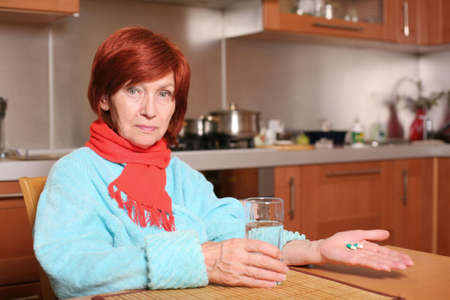 Illness grandmother holds pills and glass of waterの写真素材