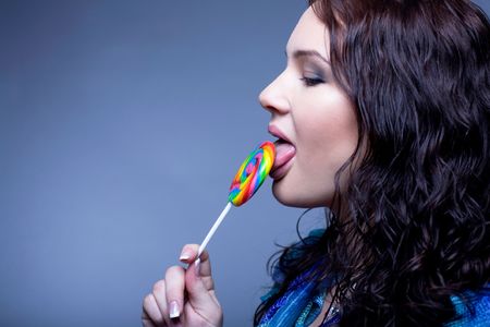 Portrait of an attractive woman with bright lollipop over blue backgroundの写真素材