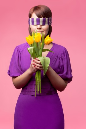 Young woman with closed eyes is holding a bunch of tulips over rose backgroundの写真素材