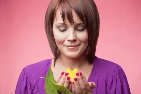 Happy woman is holding a yellow tulip over rose backgroundの写真素材