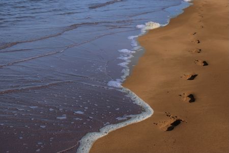 footprints left in the sand of an irish beach with the tide coming in