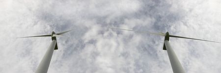 two wind turbine against a calm cloudy sky side by side