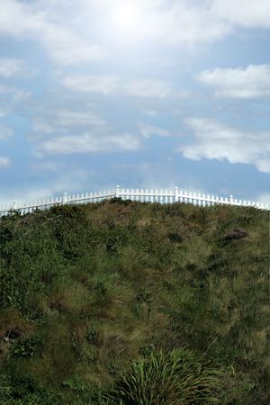 a white picket fence on top of a hill against a cloudy skyの写真素材
