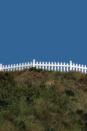 a white picket fence on top of a hill against a blue skyの写真素材